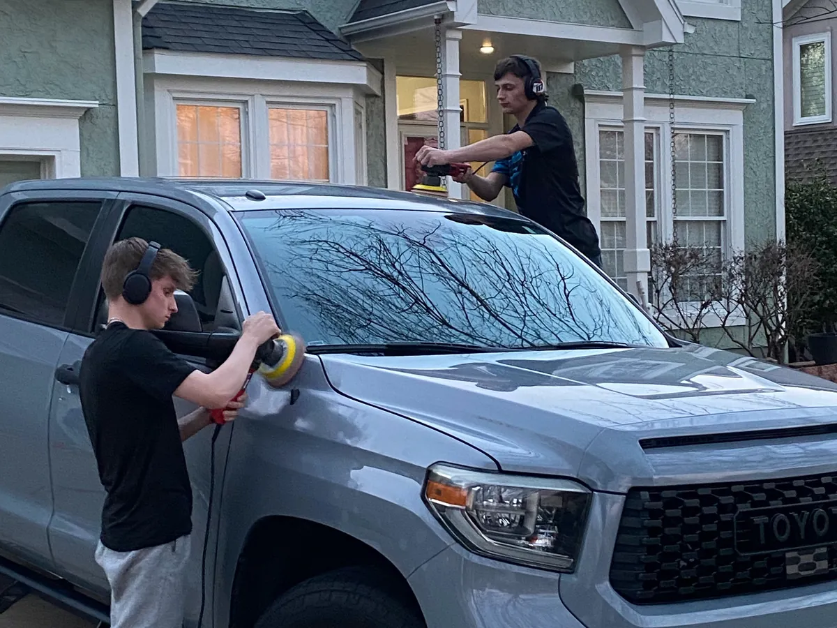 Two Aqulux techs machine-polishing a gray Toyota Tundra in a customer's driveway